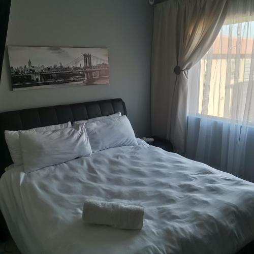 a white bed with a towel on it next to a window at Pablo and Sons Apartments in Polokwane