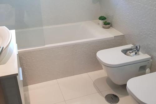 La salle de bains blanche est pourvue de toilettes et d'une baignoire. dans l'établissement Furadouro Beach Apartment, à Ovar