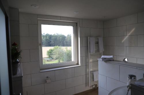 a white tiled bathroom with a window and a sink at Komfortable Ferienwohnung in der Lüneburger Heide in Sprakensehl