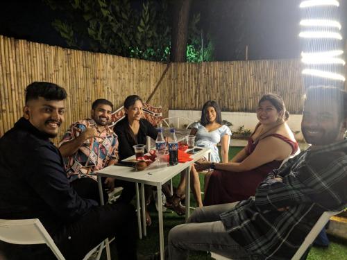 a group of people sitting around a table in a backyard at Hostell One - A complete backpacker & Coworking Hub in Pune