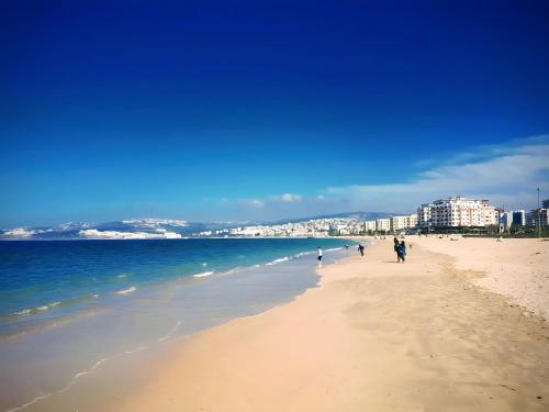 a beach with people walking on the sand and the ocean at Appartement En Bord de Mer in Tangier