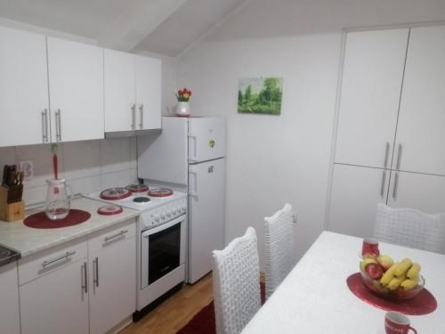 a kitchen with white appliances and a table with a bowl of fruit at Apartman Mitrovići Bajina Bašta in Bajina Bašta
