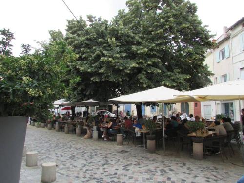 Un groupe de personnes assises à des tables sous des parasols dans l'établissement Le studio de l'artiste., à Arles