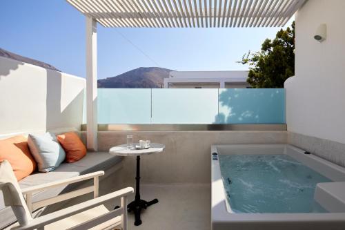 a balcony with a tub and a table and a chair at Kouros Village Hotel - Adults Only in Perissa