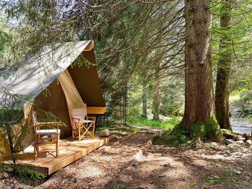 a tent in the woods with two chairs and a tree at Glamping Tent Water Village Rogla in Oplotnica