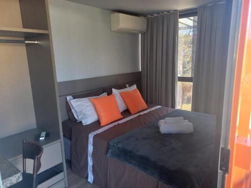 a bedroom with a bed with orange pillows and a window at Villa de Assis Suítes in Alto Paraíso de Goiás