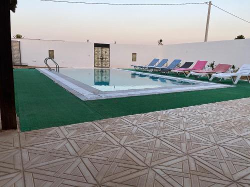 a swimming pool with chairs and a green floor at Belle Villa Avec Piscine sans vis a vis in Midoun