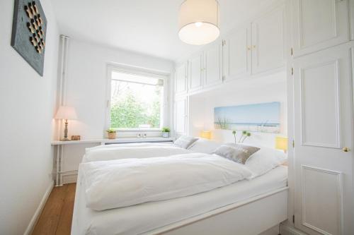 een wit bed in een witte kamer met een raam bij Sylt-to-hus-Alt-Westerland in Westerland