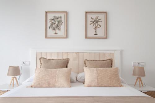 a white bedroom with a white bed with two pictures on the wall at Ítaca Apartment Peñiscola in Peñíscola