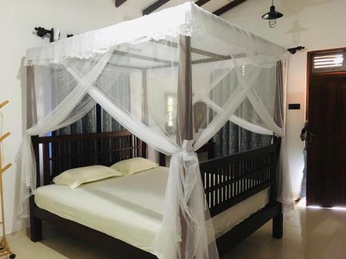 ein Schlafzimmer mit einem Himmelbett mit weißen Vorhängen in der Unterkunft Sathis villa in Ambalangoda