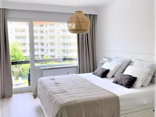 ein weißes Schlafzimmer mit einem großen Bett und einem großen Fenster in der Unterkunft Corner apartment near the sea with terrace in Blankenberge
