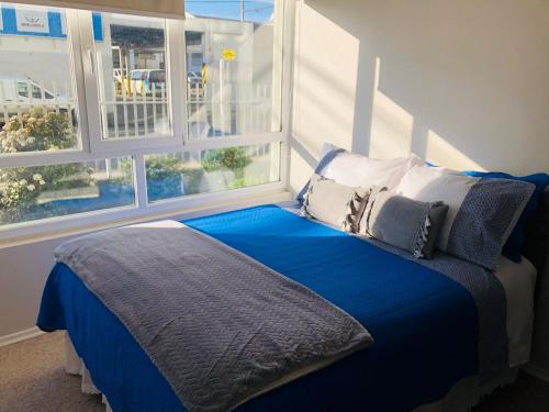 ein Bett mit blauer Bettwäsche und Kissen neben einem Fenster in der Unterkunft Acogedor departamento en Temuco in Temuco