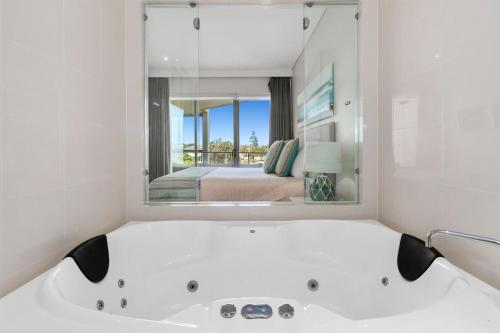 a white bathroom with a bath tub and a bedroom at Wave Culture 1204 Beach Bliss - Apartment with complex Pool & Spa in Kingscliff