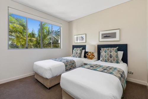 two beds in a room with a window at Wave Culture 1204 Beach Bliss - Apartment with complex Pool & Spa in Kingscliff