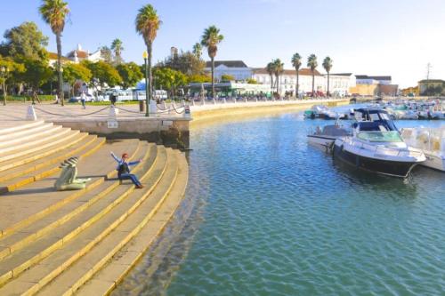 a man sitting on a bench next to a river with boats at The Islands in Faro