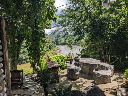een tuin met bankjes en een rivier op de achtergrond bij Baanmai Phaipa House in Sai Yok