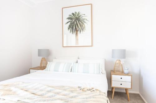 a bedroom with a white bed with a palm tree picture on the wall at Kingscliff Paradise with Ocean Views in Kingscliff