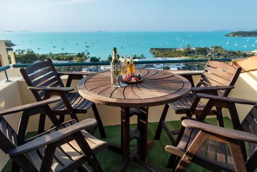 een houten tafel en stoelen op een balkon met uitzicht op de oceaan bij Bella Paradiso in Airlie Beach