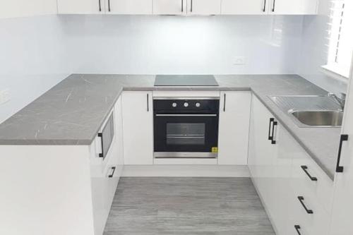 a white kitchen with a stove and a sink at LOVELY PET FRIENDLY SELF CONTAINED HOLIDAY VILLA in Bongaree