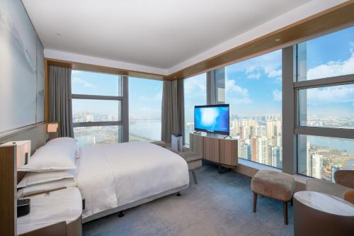 a bedroom with a bed and a tv and large windows at Four Points by Sheraton Wuhan, Jiangxia in Wuhan