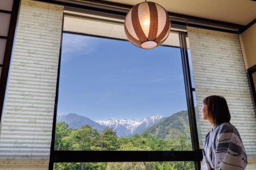 een vrouw die uit een raam naar de bergen kijkt bij Hotel Yamabuki in Komagane