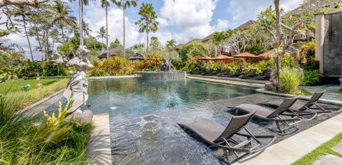 a swimming pool with two chairs and a fountain at Anumana Village Ubud in Ubud