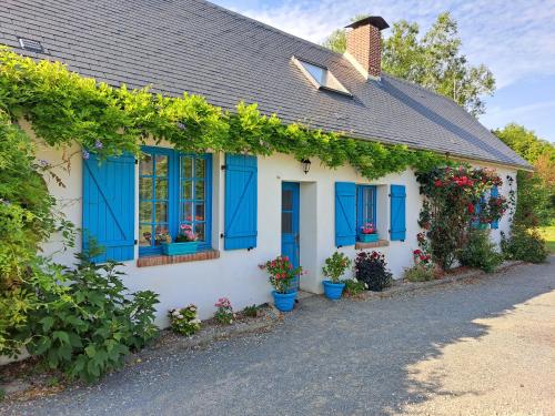 a white house with blue shutters and flowers at La maison des animaux de compagnie in Grumesnil