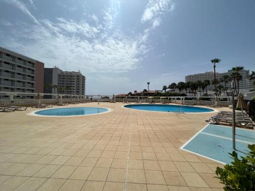 two swimming pools in a courtyard with buildings at Lookout Point Tenerife Holiday Apartment Las Americas in Playa Fañabe