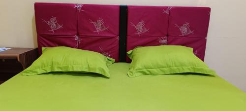 a bed with two green pillows and a purple headboard at Honey Home in Kuta Lombok