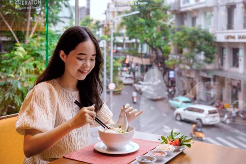 a woman sitting at a table eating a bowl of food at Sheraton Saigon Grand Opera Hotel in Ho Chi Minh City