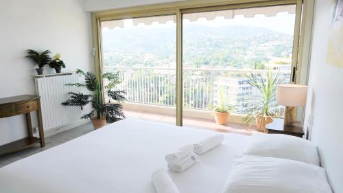 ein weißes Bett in einem Zimmer mit einem großen Fenster in der Unterkunft Cannes Marina, T3 vue Mer, Piscine, By Palmazur in Mandelieu-la-Napoule