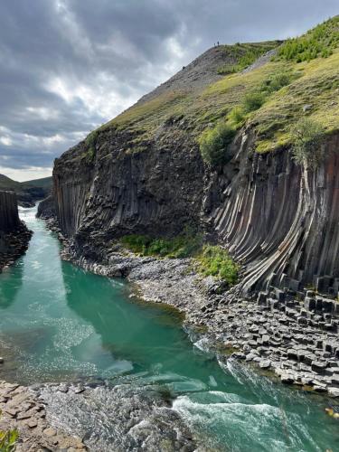 a river next to a cliff with green water at Jökla Guesthouse in Skjöldólfsstaðir