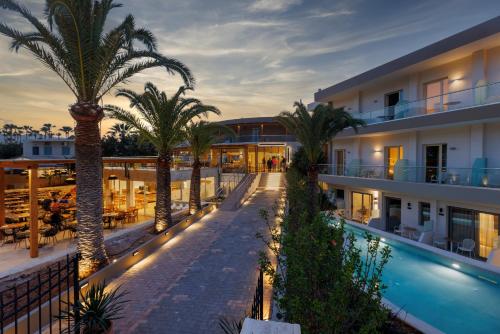 an exterior view of a hotel with palm trees and a swimming pool at Malia Bay Beach Hotel & Bungalows in Malia