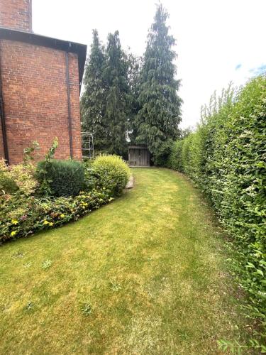 a grassy yard with a brick building and bushes at Creamore Grove Wem Shrewsbury in Wem