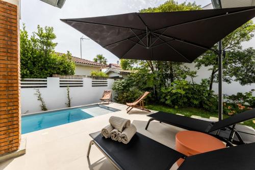 un patio avec un parasol et une piscine dans l'établissement VILLA DU GOLF - Keyweek- Villa Biarritz with swimming pool, à Biarritz