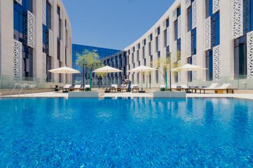 une grande piscine bleue en face d'un bâtiment dans l'établissement IntercityHotel Muscat, à Mascate