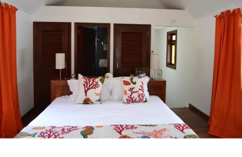 a bedroom with a large white bed with orange curtains at La Belle Tortue in Silhouette Island