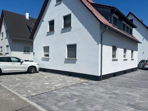 a white building with a car parked in a parking lot at 4 Zimmer Ferienwohnung am Bodensee in Friedrichshafen
