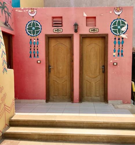 zwei Holztüren in einem rosa Gebäude mit Treppen in der Unterkunft Sahara Pyramids Hotel 