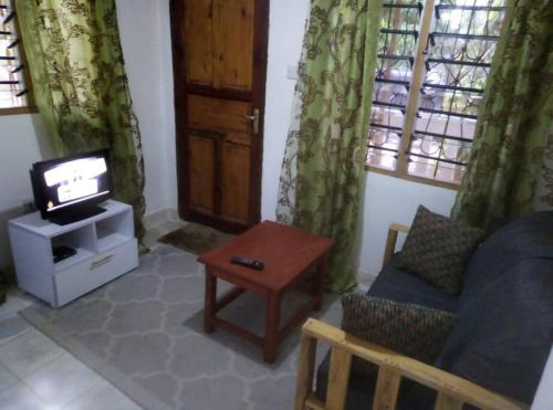 een woonkamer met een tv en een bank en een tafel bij Moringa Garden Cottage, mombasa, north coast, kikambala in Mtwapa