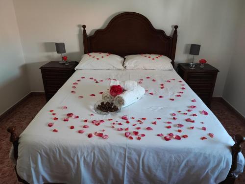 a bed covered with red roses on a white blanket at Apartamentos Guiomar Campos in Porto Covo