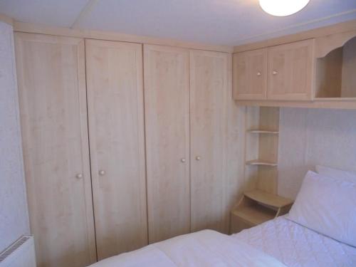 a bedroom with wooden cabinets and a white bed at Seaview: The Crown:- 6 Berth, Central heated, Enclosed Veranda in Ingoldmells