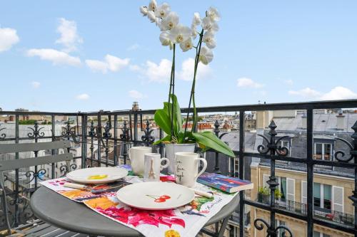 une table avec des assiettes et un vase de fleurs sur le balcon dans l'établissement Appartement des Sèvres - Welkeys, à Paris