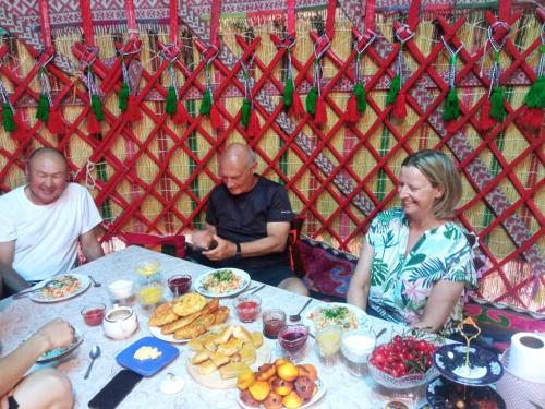 um grupo de pessoas sentadas à volta de uma mesa com comida em Green guest house em Bokonbayevo