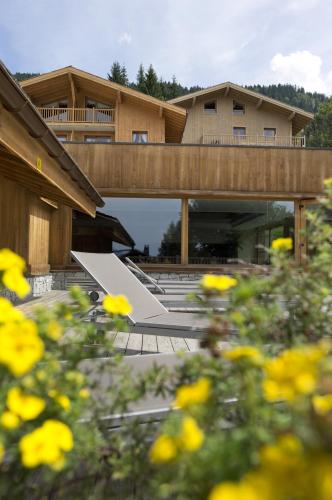 un bâtiment avec un pont aux fleurs jaunes en avant dans l'établissement CGH Résidences & Spas Les Chalets de Jouvence, aux Carroz d'Arâches