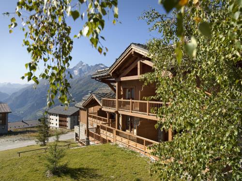 une maison en rondins avec un balcon et des montagnes en arrière-plan. dans l'établissement CGH Résidences & Spas Les Cimes Blanches, à La Rosière