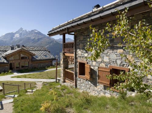un bâtiment en pierre avec une montagne en arrière-plan dans l'établissement CGH Résidences & Spas Les Cimes Blanches, à La Rosière