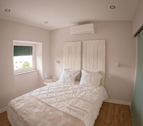 a bedroom with a bed with white sheets and a window at Casa do Bairro in Seia