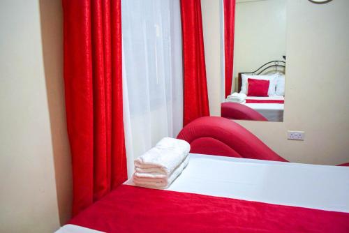 Casabella Apartment - Pristine Homes,Tom Mboya في كيزيمو: غرفة نوم مع ستائر حمراء وسرير مع مرآة