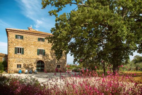 un gran edificio de piedra con flores rosas delante de él en Villa Le Prata - Farm House & Winery - Adults Only, en Montalcino